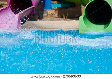 Two Colorful Pipes At The Waterpark, Pool And Splases Of The Water Around.
