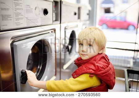 A Little Boy Loads Clothes Into The Washing Machine In Public Laundrette