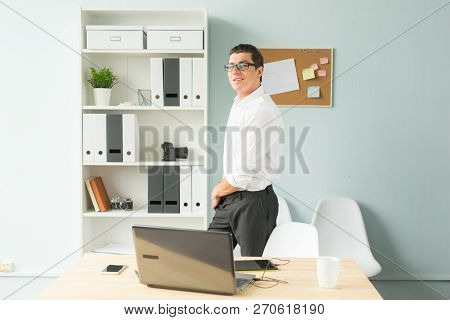 Business, Office, People Concept - Handsome Man In Glasses Stands In The Office Near A Computer And 