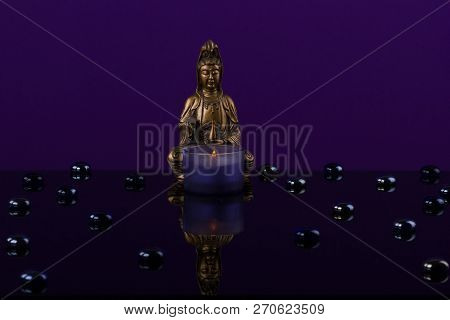 Buddha Of Bronz In Meditation With Candle On The Itense  Violet Background.