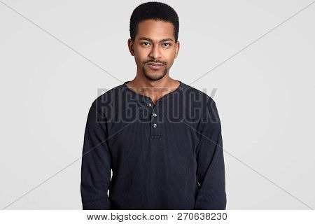 Waist Up Shot Of Black Man With Short Curly Hair, Little Beard, Looks Seriously At Camera, Thinks Ab