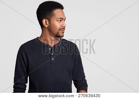 Shot Of Dark Skinned Man Stands Sideways At Camera, Notices Something On Free Space, Has Serious Exp