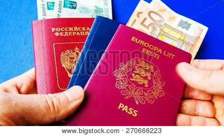Persons Hand Holding Passports On Blue Background. Citizenship Of Estonia And Russia. Citizenship Of