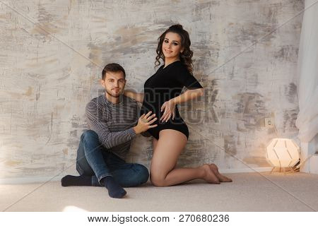Happy Man Put His Handr On The Belly Of His Pregnant Wife. Young Family In Studio. Couple Wait For A