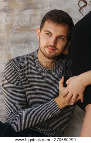 Happy Man Put His Handr On The Belly Of His Pregnant Wife. Young Family In Studio. Couple Wait For A