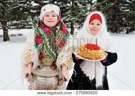 Two Little Girls In Fur Coats And Shawls In Russian Style On His Head Against The Background Of A Sa