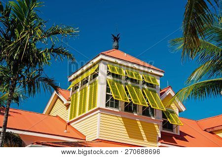 Mansard With Open Yellow Window Shutters And Pineapple On Terracotta Roof On Sunny Day On Blue Sky I