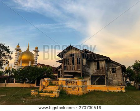 Old abandoned traditional malay house with a mosque in the background