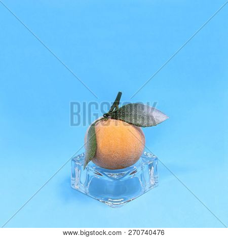 Frozen Mandarin On Ice Cube On Blue Background. Creative Concept: Quickly Frozen Fruits And Vegetabl
