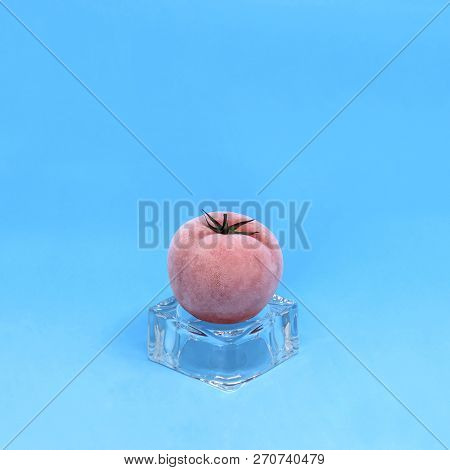 Frozen Tomato On Ice Cube On Blue Background. Creative Concept: Quickly Frozen Fruits And Vegetables