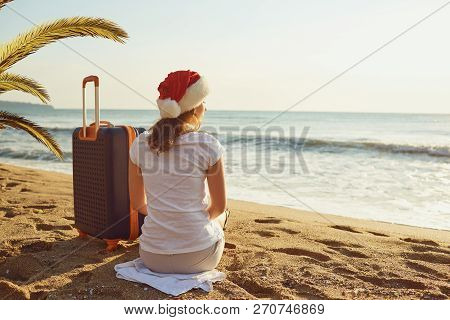 A Girl In A Santa Claus Hat With A Suitcase On The Beach On Chri
