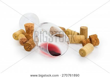 Wine Glass Lying On Its Side With Small Amount Of Red Wine Among Of Different Wine Cork On A White B