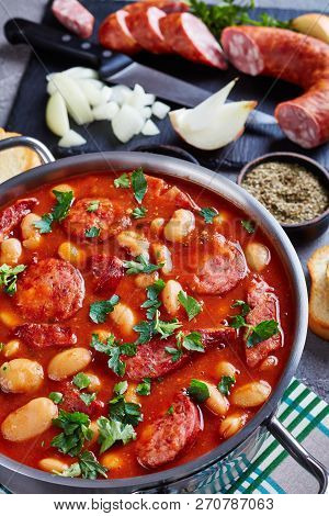 Hearty Beans Stew With Sausages, Herbs And Spices In Tomato Sauce In A Metal Casserole On A Concrete
