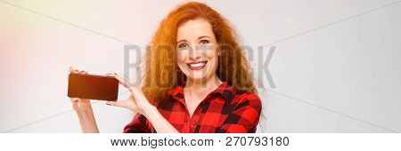 Young Red-haired Girl In A Red Checkered Shirt. Young Girl Holding A Phone