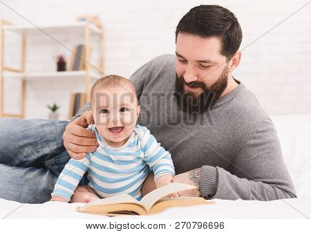 Young Man Babysitting. Bearded Father Reading Book To His Adorable Baby Son