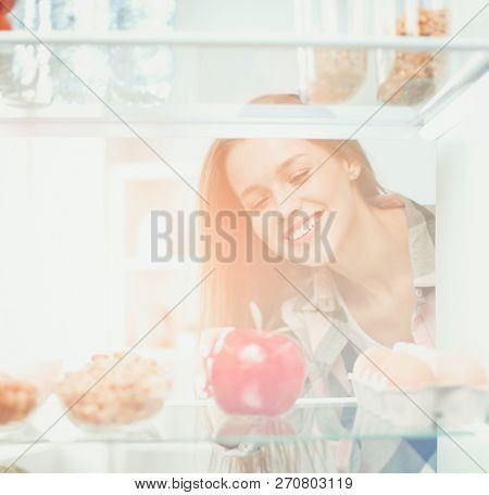 Portrait of female standing near open fridge full of healthy food, vegetables and fruits. Portrait of female