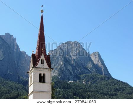 Bell Tower Of The Church Of St Maria Ausiliatrice Against The Dolomites . Siusi Allo Sciliar, South 