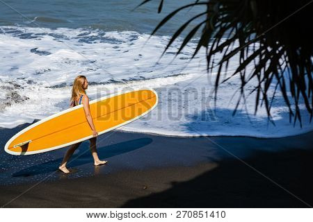 Sporty Girl In Bikini With Surf Board Walk On Black Sand Beach. Young Surfer Woman Run By Water Pool
