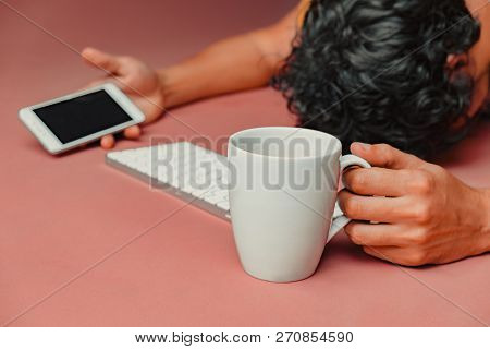 Man Has Burn Out At Work. Head, Keyboard, Smart Phone And Coffee On Pink Table