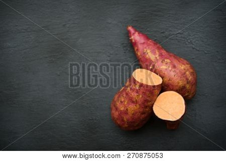 Raw orange sweet potatoes close up on dark background. Copy space top view.