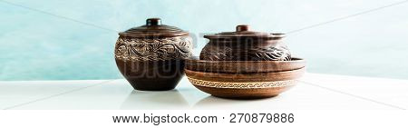 Pots And Plates Of Clay On A White Table And A Blue Background. Clay Pottery Kitchen Utensils Made B