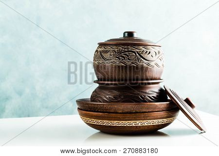 Pots And Plates Of Clay On A White Table And A Blue Background. Clay Pottery Kitchen Utensils Made B