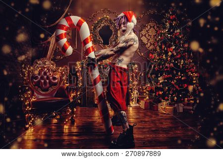 Bad Santa concept. Portrait of a nude tattooed Santa with purple dreads demonstrating antisocial behavior, rudeness and aggression. 