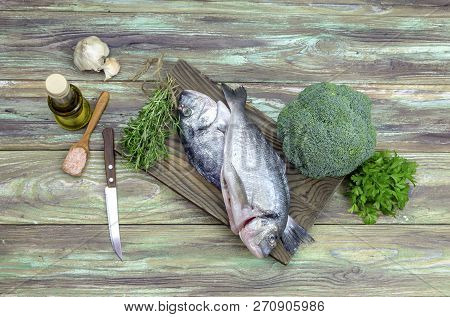 Fish Sea Breams(sparus Aurata) On A Cutting Board, Olive Oil, Broccoli, Garlic And Aromatic Herbs On