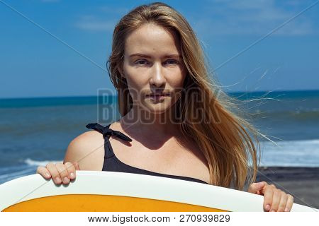 Surfer Girl In Bikini With Surfboard Posing On Black Sand Beach. Face Portrait. Young Woman Look At 