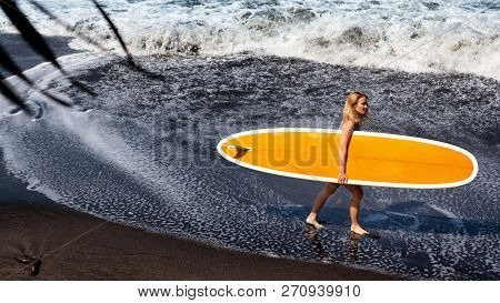 Sporty Girl In Bikini With Surf Board Walk On Black Sand Beach. Young Surfer Woman Run By Water Pool
