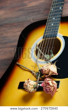 Acoustic Guitar With Dried Roses On The Wooden Table. Template For Advertising A Concert Of Memory W