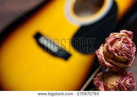 Acoustic Guitar With Dried Roses On The Wooden Table. Template For Advertising A Concert Of Memory O