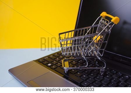 E-commerce, Concept. Online Shopping, Shopping Cart On Laptop Keyboard. Yellow Background