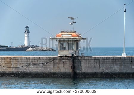 A Small Bulit Structure On A Pier With The Darling Pier Lighthouse In The Background On Fushan Bay I