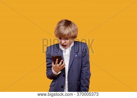 A Frightened Blond Boy With A Frightened Face Looks Into His Phone.