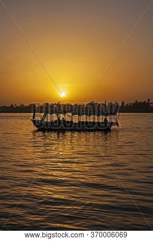 Traditional Egyptian Felluca River Boat Sailing On The Nile River Bank With Sunset And Reflection In