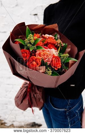 Bouquet Of Flowers In Burgundy Package In The Hands Of A Woman Florist On Background A White Brick W