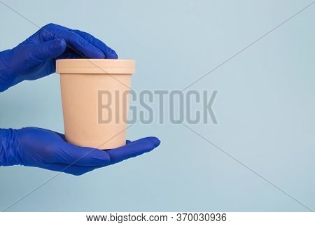 Womans Hands In Blue Disposable Protective Gloves On Pastel Blue Background Holding Round Paper Food
