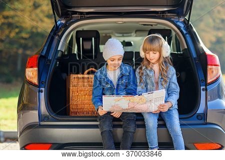 Agreeable Boy And Girl Are Looking At The Road Map While Sitting In The Autos Trunk And Discussing T