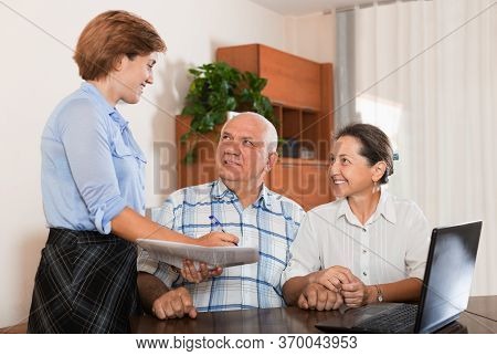 Mature Couple Answer Questions Of Outreach Worker With Notebook In Office