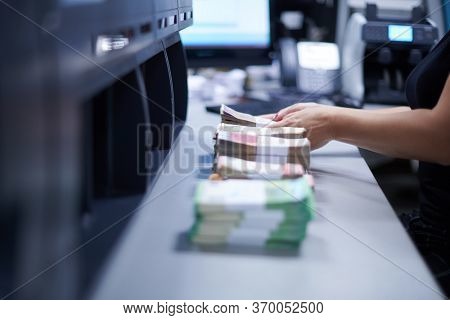 Bank employees using money counting machine while sorting and counting paper banknotes inside bank vault. Large amounts of money in the bank