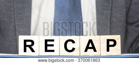Recap Word From Wooden Blocks On Desk Board With Man In Suit On Background. Business Recap Concept