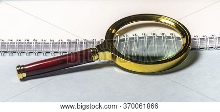 Close Up Golden Magnifying Glass Loupe With Red Wooden Handle On White Planner Or Notebook And Gray 