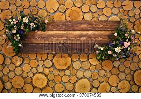 Wooden Board With Flowers On A Background Of Round Log Cabins With Space For Text.