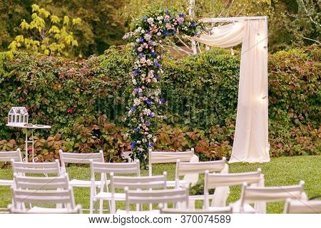 Wedding. Ceremony. Wedding Arch. Wedding Arch Of Flowers And Greenery Stands On The Green Grass In T