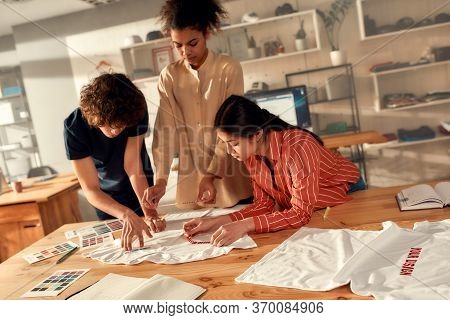 Creative People Trying On Stickers With Text, While Discussing Logo And Design Of T-shirt. Young Man