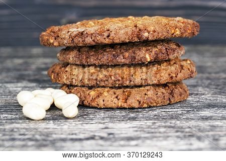 A Stack Of Oatmeal Cookies With Crushed Roasted Peanuts And Lying On A Wooden Table Next To Whole Nu