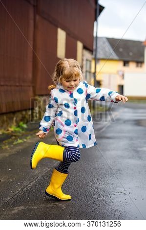 Little Toddler Girl Wearing Yellow Rain Boots, Running And Walking During Sleet On Rainy Cloudy Day.