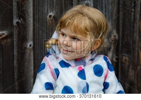 Outdoor Portrait Of Happy Smiling Little Toddler Girl Wearing Rain Jacket On Rainy Cloudy Day. Cute 