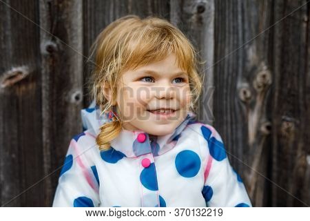 Outdoor Portrait Of Happy Smiling Little Toddler Girl Wearing Rain Jacket On Rainy Cloudy Day. Cute 